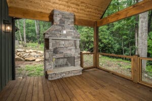 Covered patio with stone fireplace and forest view.